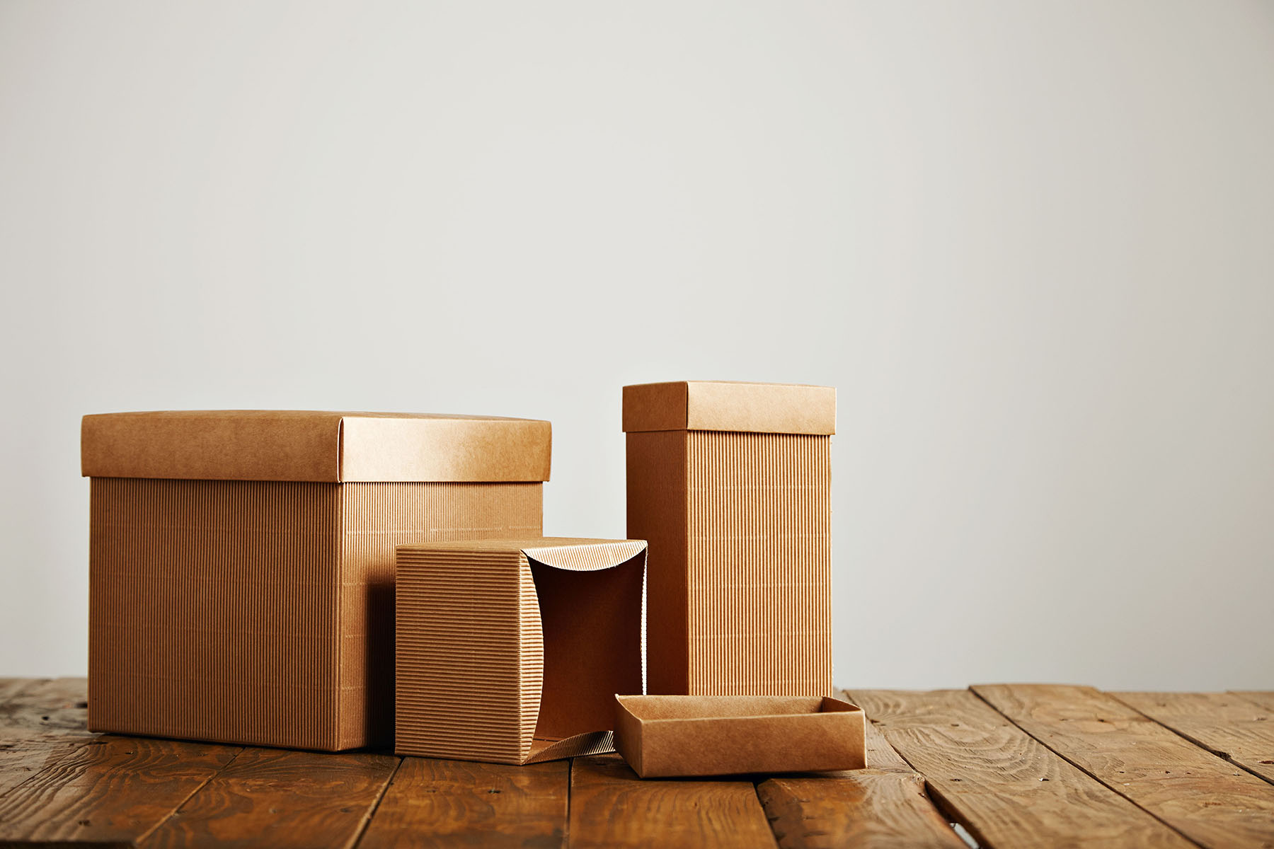 Mockups of blank brown corrugated cardboard boxes Unlabeled similar boxes of different shapes and sizes on an uneven wooden table isolated on white